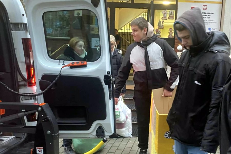 Osoby stoją przy samochodzie dostawczym i wyjmują rzeczy.