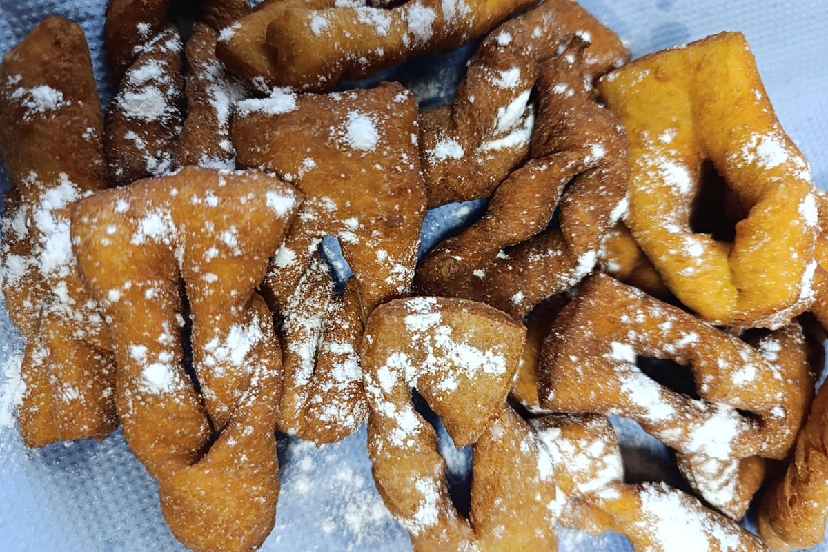 Gotowe smażone kawałki ciasta posypane cukrem pudrem, podane na talerzu obok chrupiących fawork&oacute;w.